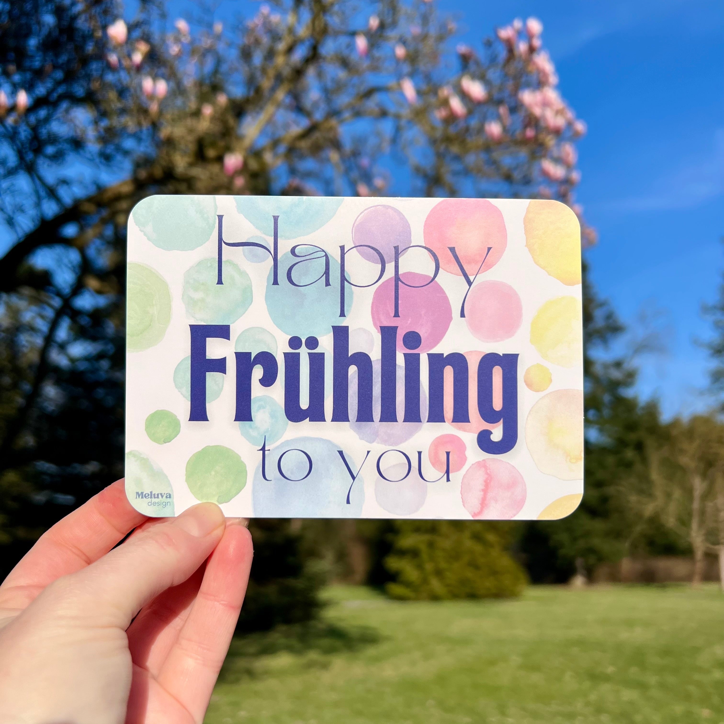 Die Postkarte mit dem Schriftzug Happy Frühling to You vor einem Magnolien-Baum