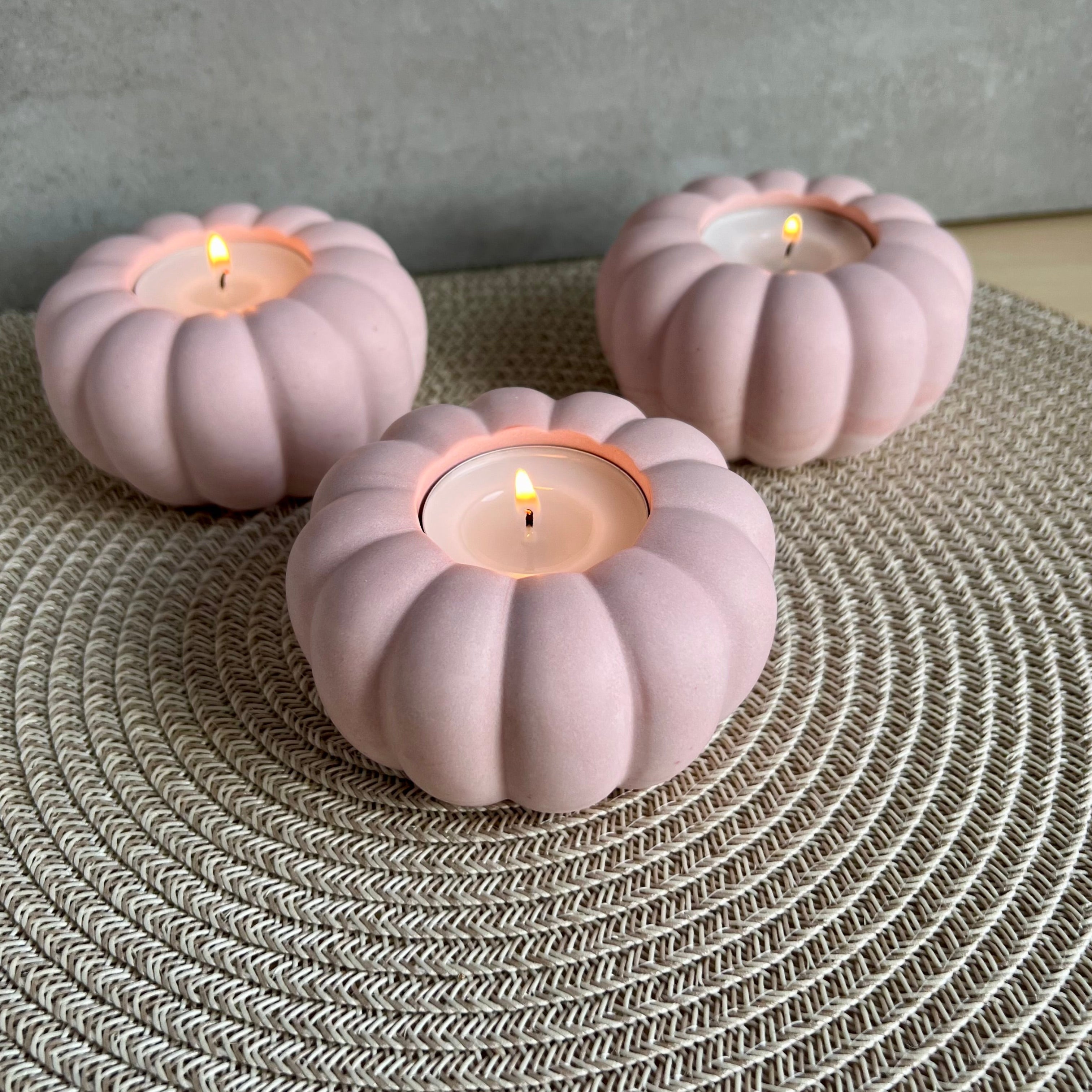 Drei Teelicht-Halter in rosa, die Form erinnert an eine Blume oder einen Kürbis. 