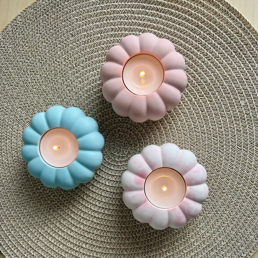 Drei Teelicht-Halter in rosa marmoriert, rosa und blau. die Form erinnert an eine Blume oder einen Kürbis. 