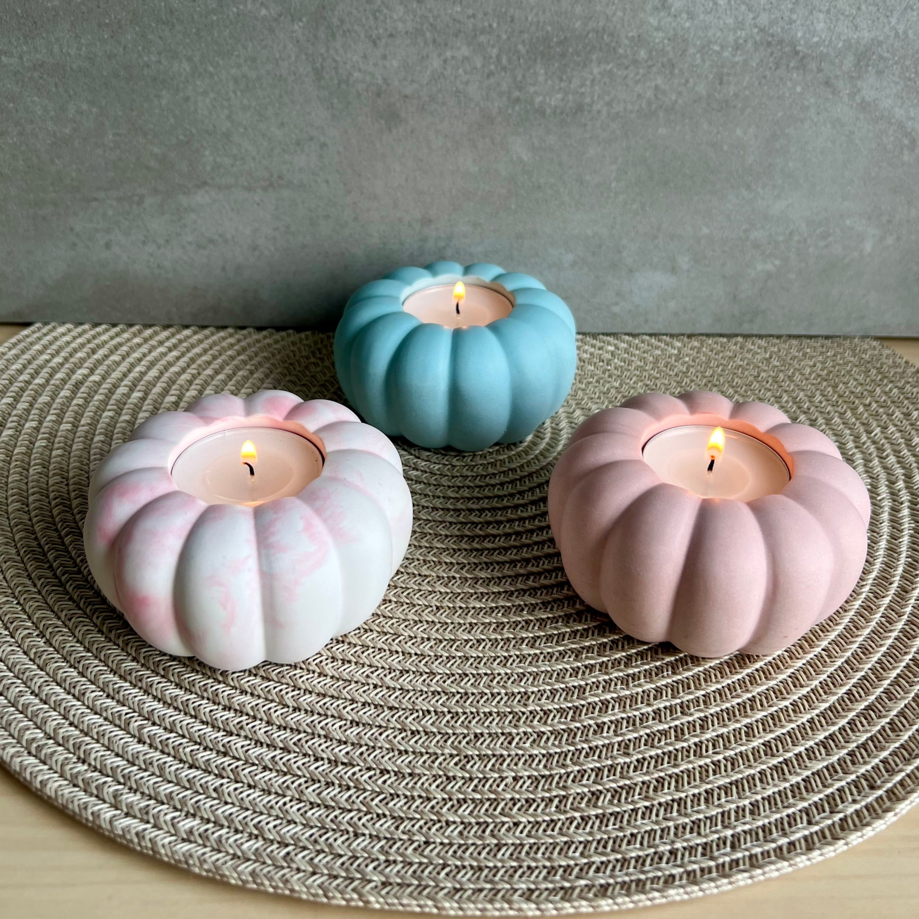 Drei Teelicht-Halter: in rosa marmoriert, blau und rosa. die Form erinnert an eine Blume oder einen Kürbis. Sie sind im Dreieck aufgestellt.