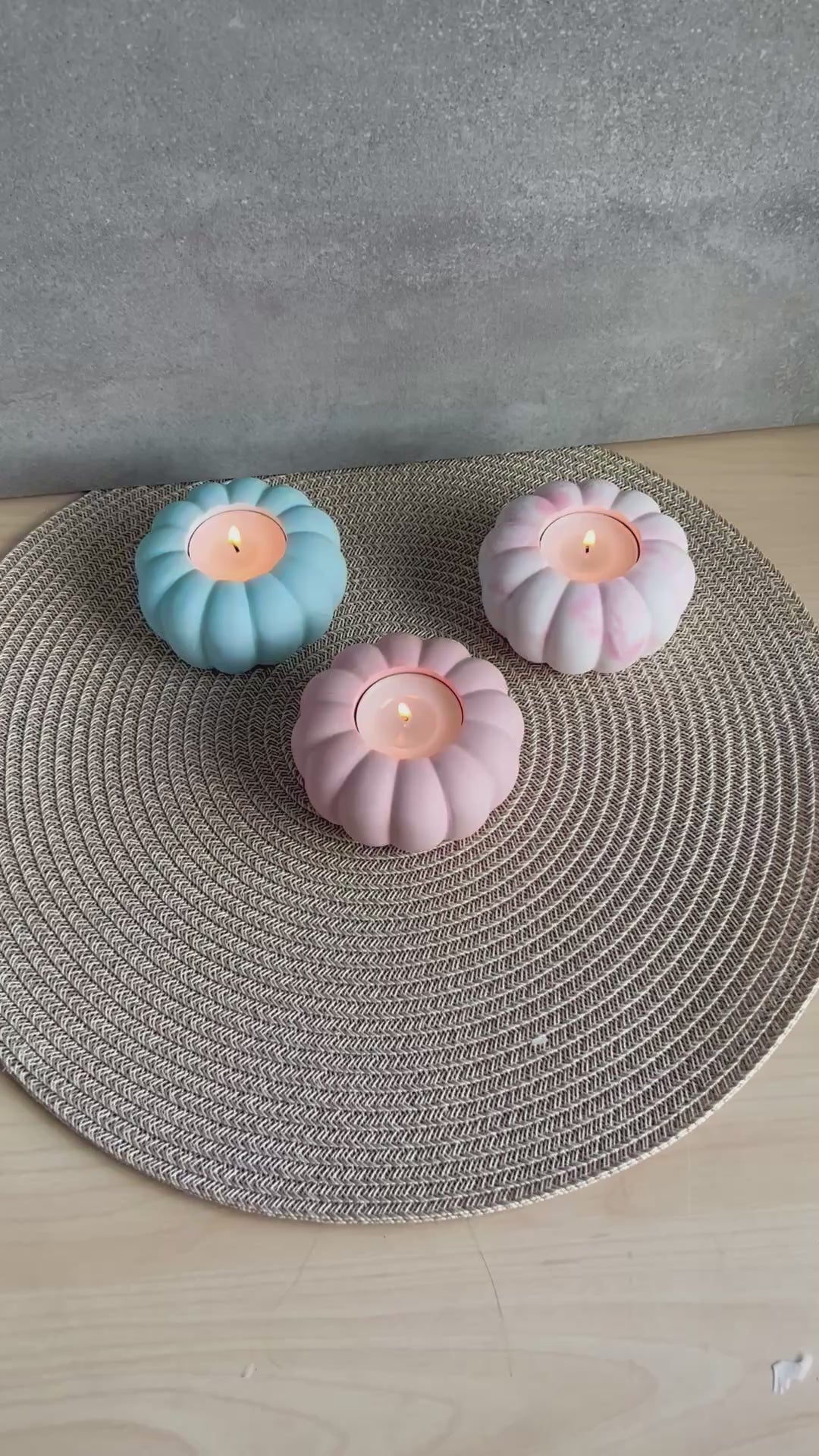 Ein Video wo man drei Teelichthalter sieht in zeitloser Blüten-Form, rosa, blau und rosa marmoriert. Die Kamera zoomt in den mittleren, rosanen, Teelicht-Halter hinein. In allen drei brennen Teelichter. 